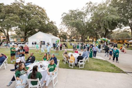 a group of people enjoying a pic nic on a green lawn with white tables and chairs